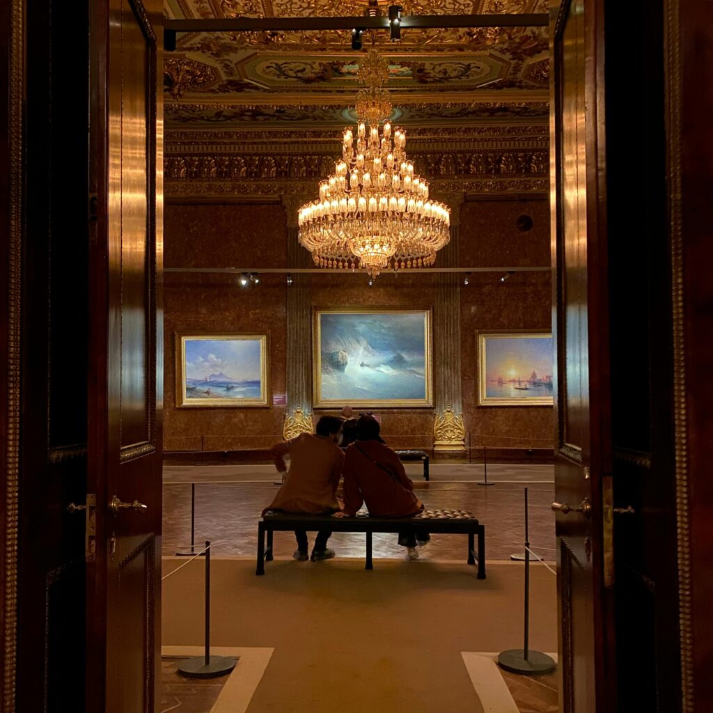 Visitors admire paintings under an ornate chandelier in a luxurious art gallery in İstanbul.
