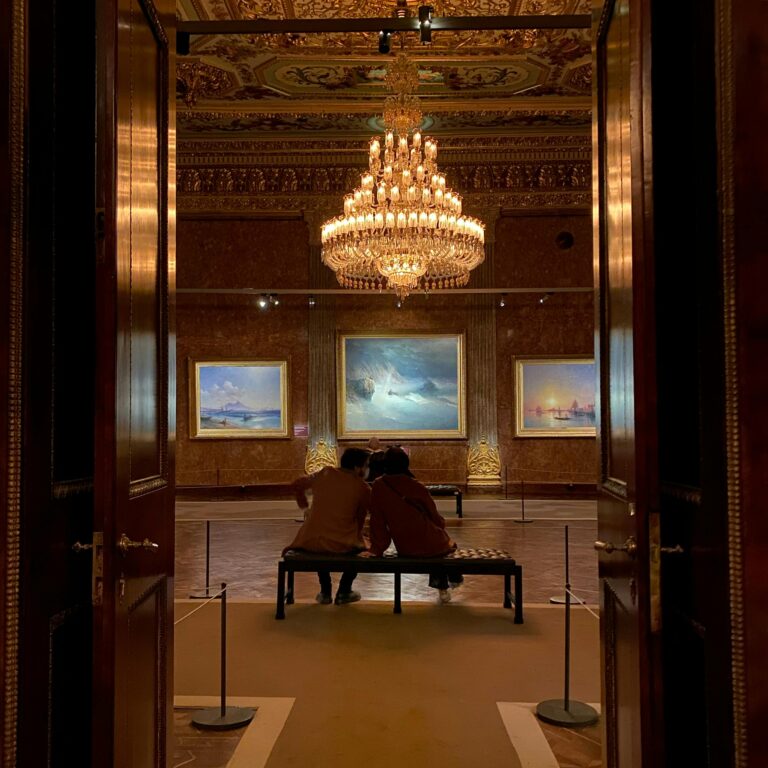 Visitors admire paintings under an ornate chandelier in a luxurious art gallery in İstanbul.