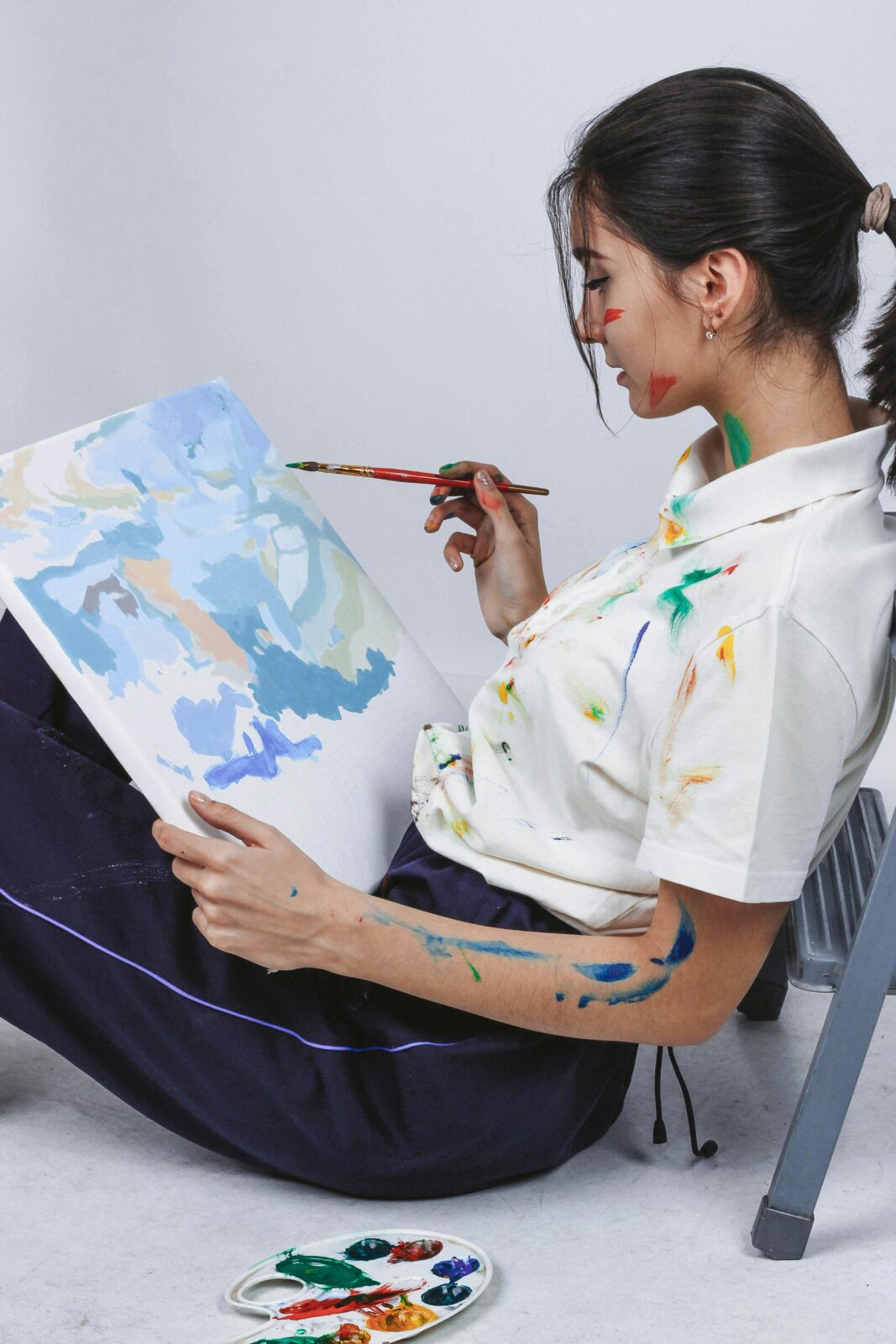 Side view of a young female artist painting abstract art on canvas, emphasizing creativity and artistry.